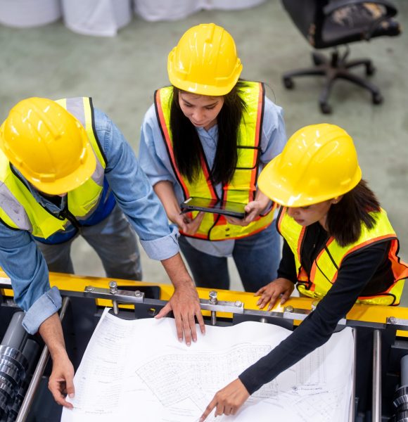 High-angle view from above of an architect, foreman and construction worker examining a blueprint in a construction of manufacturing site.